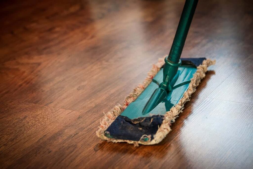 Maid service concept depicted by a green-handled mop on a wooden floor.