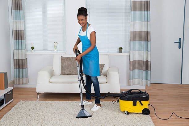 Woman in apron vacuuming room, providing House Cleaning Services.