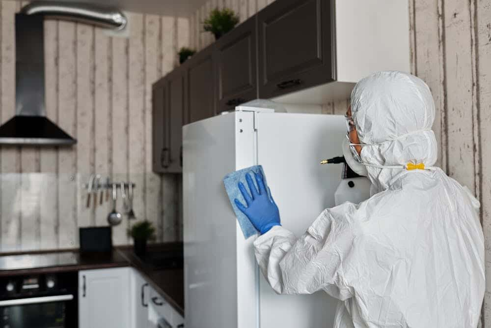 A person in a white protective suit cleaning a refrigerator during house cleaning.