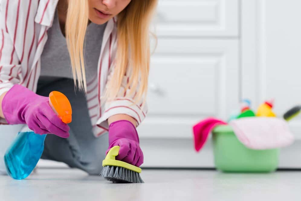 A woman engaged in house cleaning sweeps the floor with a broom, maintaining cleanliness.