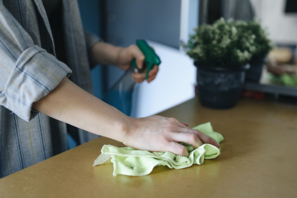A person cleaning a table with a cloth and spray bottle
