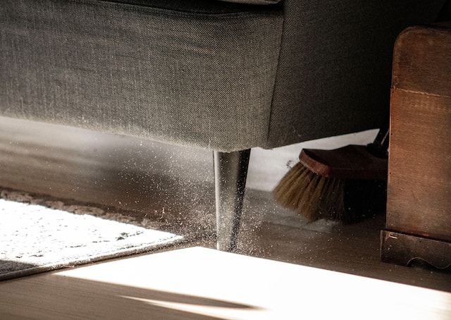 Broom under couch sweeping out dust