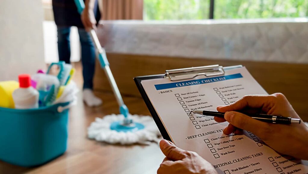 Hands check off a cleaning checklist, while a person mops the floor.