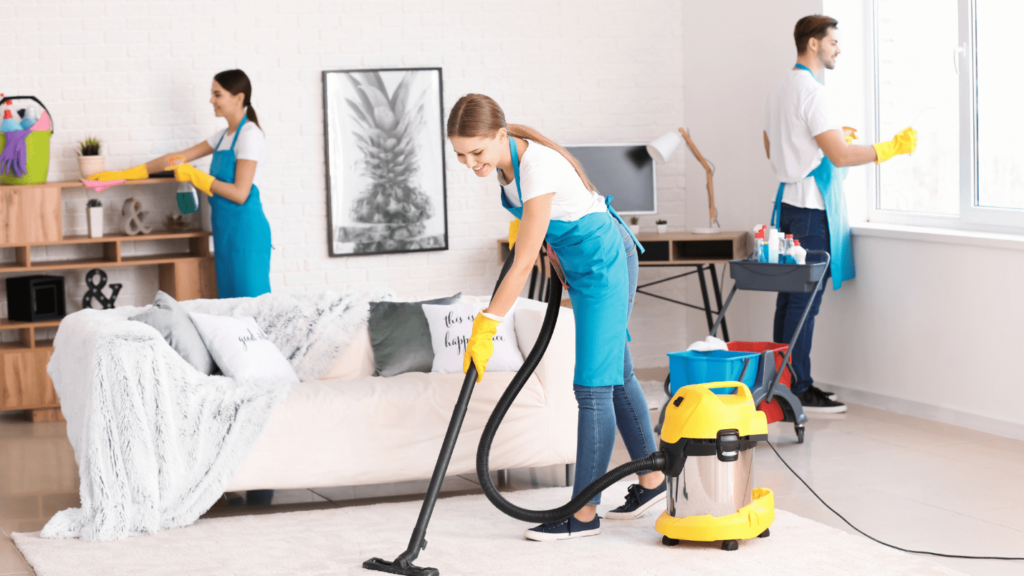 Three cleaners wearing gloves and aprons clean a living room.